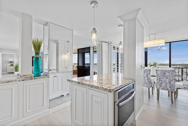 kitchen featuring white cabinetry, light hardwood / wood-style floors, hanging light fixtures, and stainless steel oven