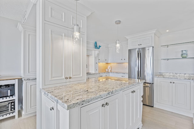 kitchen with hanging light fixtures, stainless steel fridge, white cabinets, and backsplash