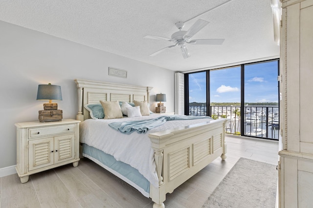 bedroom with expansive windows, light hardwood / wood-style flooring, a textured ceiling, and ceiling fan