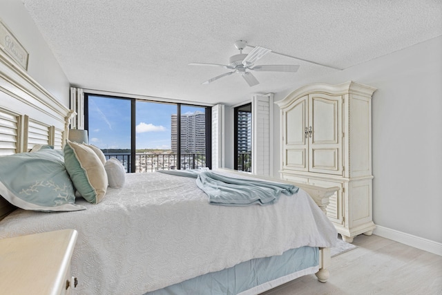 bedroom featuring ceiling fan, a textured ceiling, light wood-type flooring, and a wall of windows