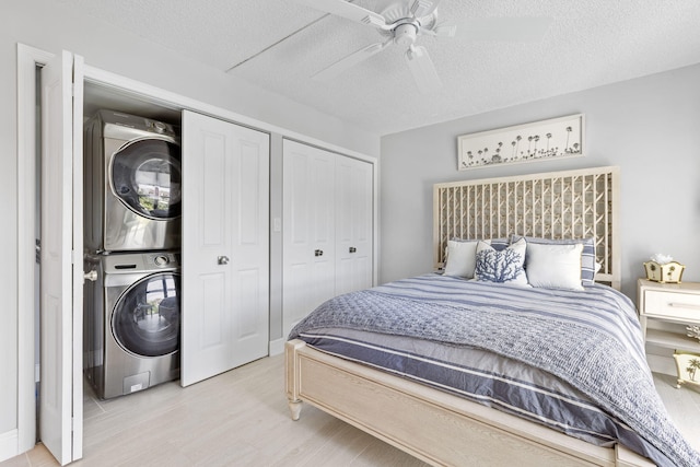 bedroom with ceiling fan, a textured ceiling, stacked washer and dryer, and light hardwood / wood-style flooring