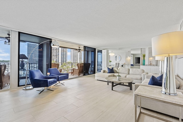 living room featuring light wood-type flooring, a wall of windows, ceiling fan, and a textured ceiling