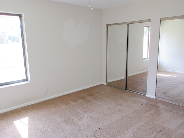 unfurnished bedroom featuring multiple closets, multiple windows, and light carpet