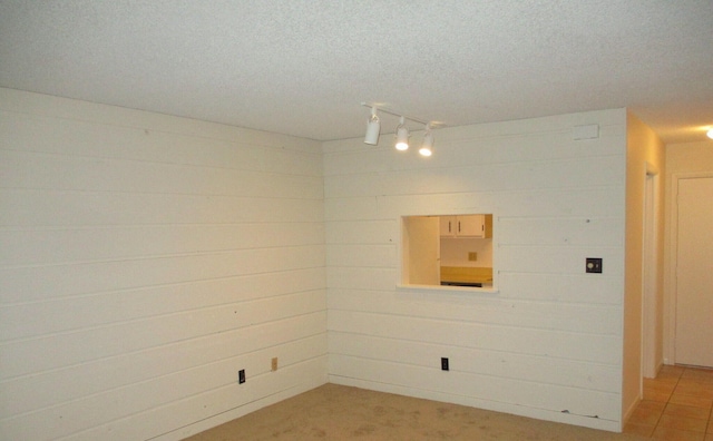 spare room with a textured ceiling, rail lighting, and wooden walls