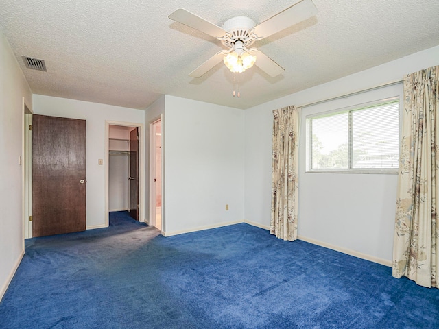 unfurnished bedroom featuring a closet, a spacious closet, dark carpet, a textured ceiling, and ceiling fan