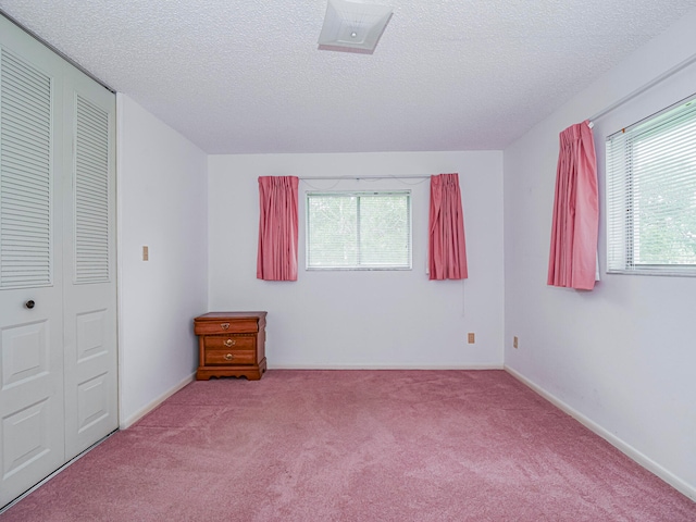 unfurnished bedroom featuring a closet, multiple windows, a textured ceiling, and light carpet