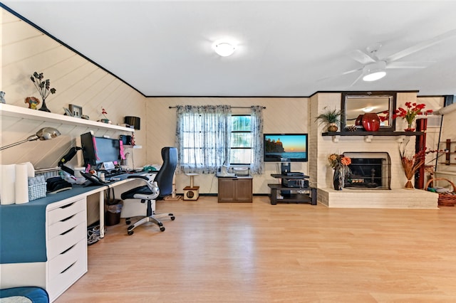 office with ceiling fan, wood walls, a fireplace, and light hardwood / wood-style flooring