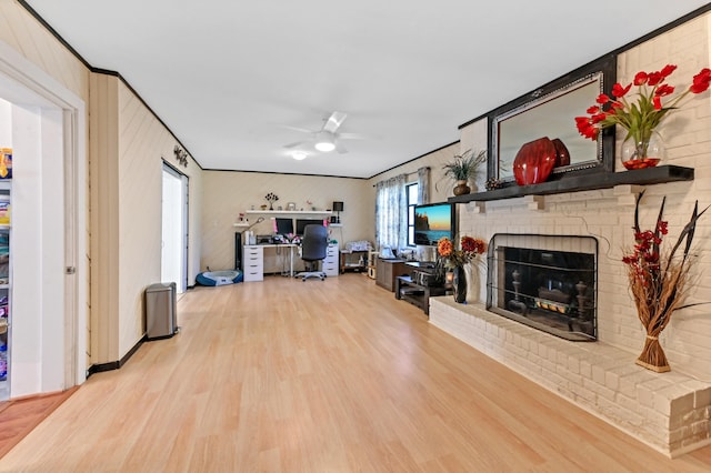 living room with light wood-type flooring, a brick fireplace, ceiling fan, and ornamental molding