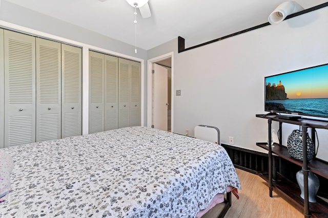 bedroom with light hardwood / wood-style floors, ceiling fan, and multiple closets