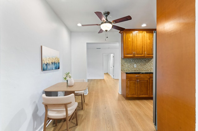 kitchen featuring light wood-type flooring, ceiling fan, dark stone counters, and backsplash