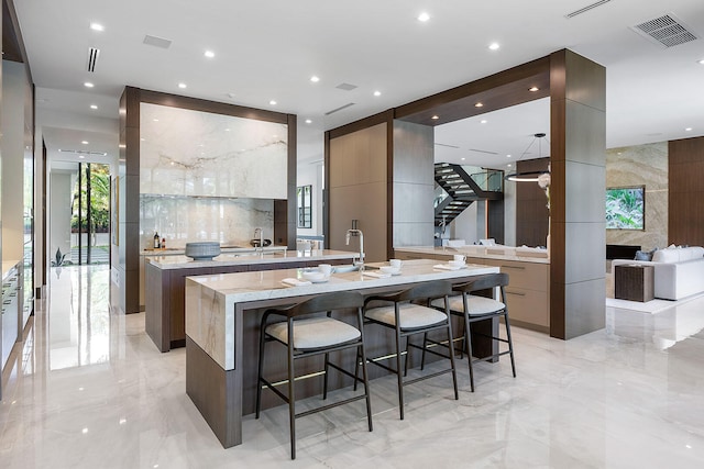 kitchen featuring a kitchen bar, light stone counters, tile walls, and an island with sink