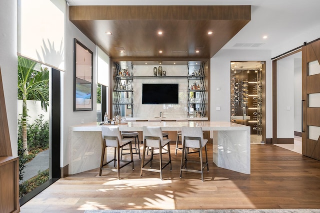 bar with decorative backsplash, light hardwood / wood-style floors, and a barn door