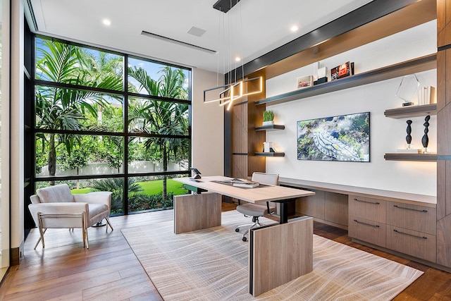 home office with built in desk, expansive windows, and light hardwood / wood-style floors