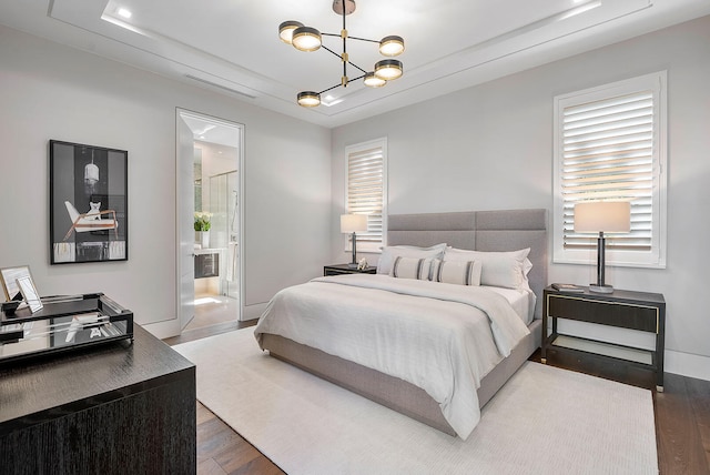 bedroom featuring a chandelier, dark hardwood / wood-style flooring, and connected bathroom