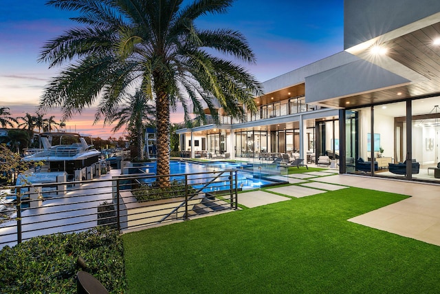 pool at dusk with a patio area and a yard