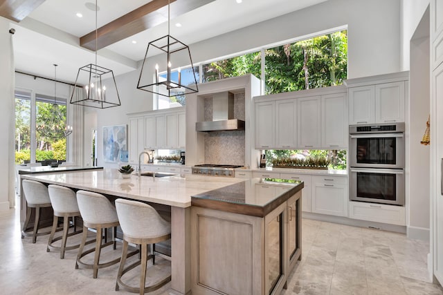 kitchen featuring light stone countertops, sink, wall chimney exhaust hood, a large island with sink, and appliances with stainless steel finishes