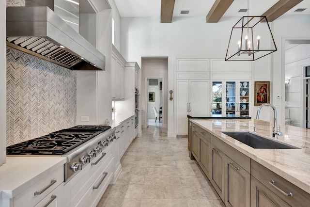 kitchen with sink, wall chimney exhaust hood, light stone counters, decorative light fixtures, and white cabinets