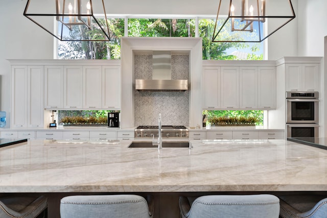 kitchen featuring backsplash, double oven, decorative light fixtures, light stone counters, and a breakfast bar area