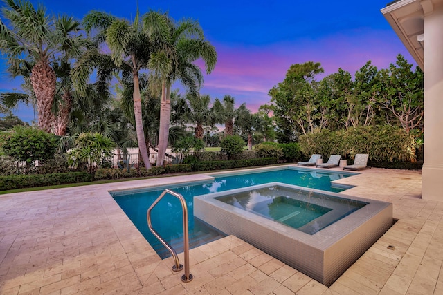 pool at dusk with a patio area and an in ground hot tub