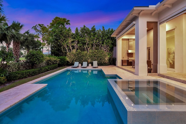 pool at dusk featuring an in ground hot tub and a patio