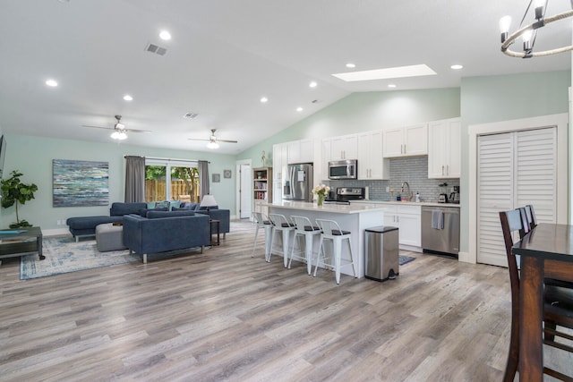 kitchen featuring a skylight, white cabinetry, stainless steel appliances, a kitchen bar, and a kitchen island