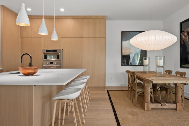 kitchen featuring light hardwood / wood-style flooring, sink, pendant lighting, a center island with sink, and light brown cabinetry