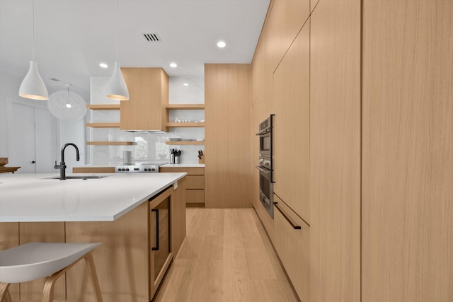 kitchen with light wood-type flooring, sink, light brown cabinets, a center island with sink, and hanging light fixtures