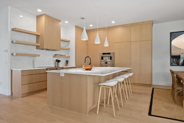 kitchen featuring light hardwood / wood-style flooring, pendant lighting, decorative backsplash, an island with sink, and light brown cabinetry