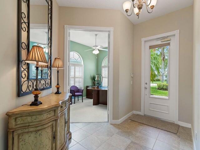 entryway featuring ceiling fan with notable chandelier, light tile patterned flooring, and baseboards