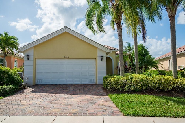 view of front of property featuring a tiled roof, decorative driveway, an attached garage, and stucco siding