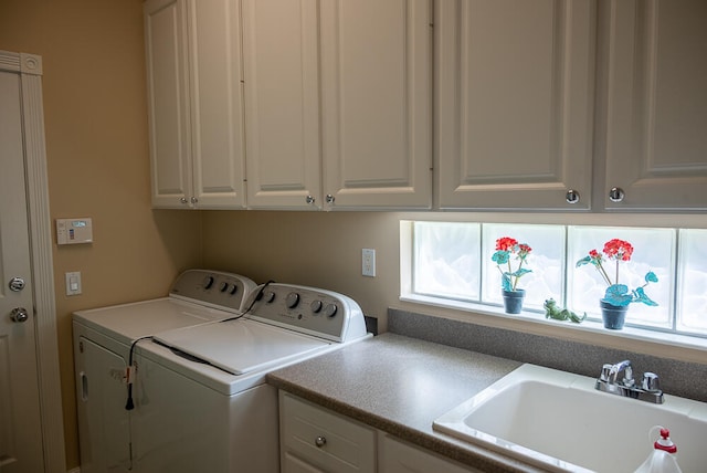 clothes washing area featuring a healthy amount of sunlight, cabinet space, washing machine and dryer, and a sink