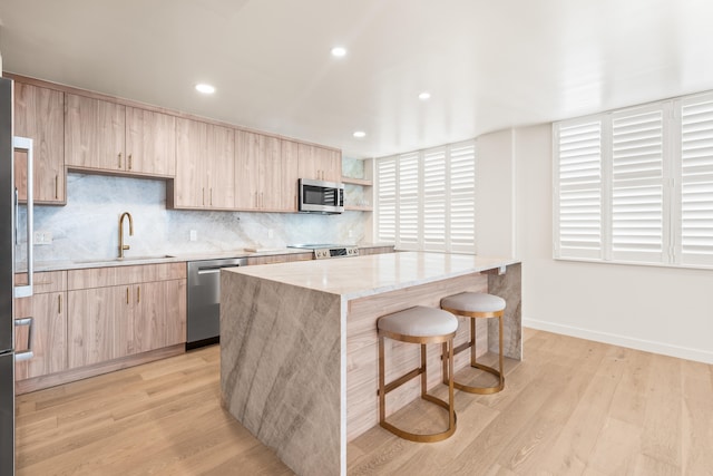 kitchen with sink, a breakfast bar, stainless steel appliances, a center island, and light stone counters