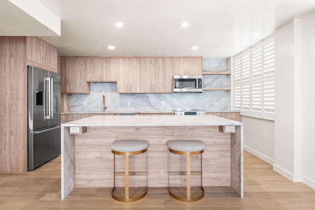 kitchen featuring a kitchen island, appliances with stainless steel finishes, decorative backsplash, and light hardwood / wood-style flooring