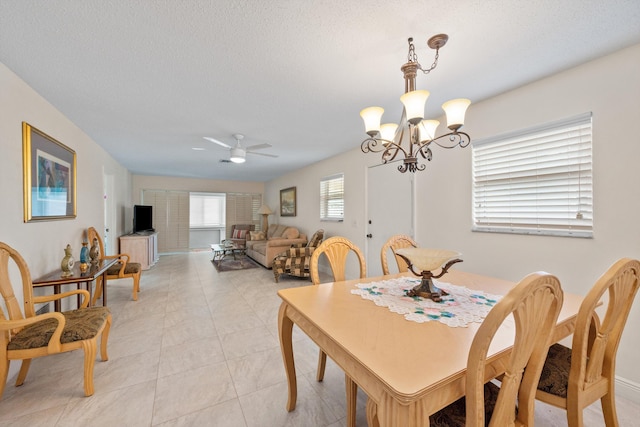 dining area with a textured ceiling, light tile patterned floors, and ceiling fan with notable chandelier