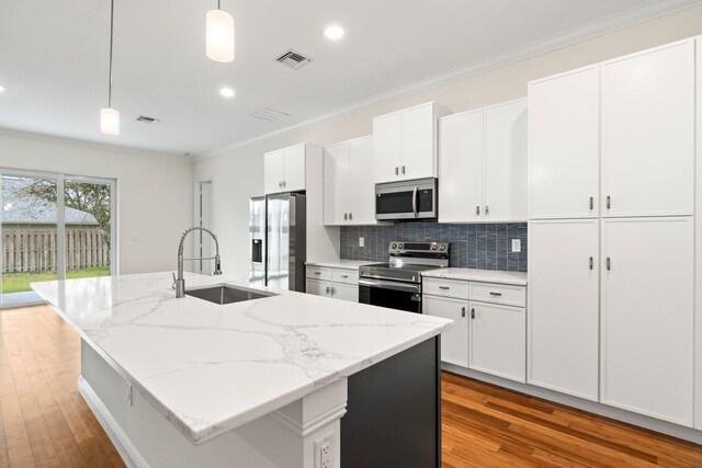 kitchen with a center island with sink, white cabinetry, light hardwood / wood-style flooring, hanging light fixtures, and appliances with stainless steel finishes