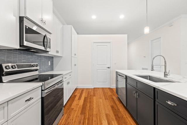 kitchen with stainless steel appliances, light wood-type flooring, pendant lighting, white cabinets, and sink