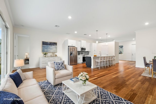 living room featuring visible vents, baseboards, light wood-type flooring, ornamental molding, and recessed lighting