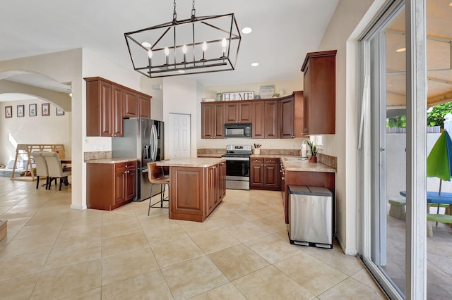 kitchen with light stone countertops, a breakfast bar, stainless steel appliances, a notable chandelier, and a kitchen island