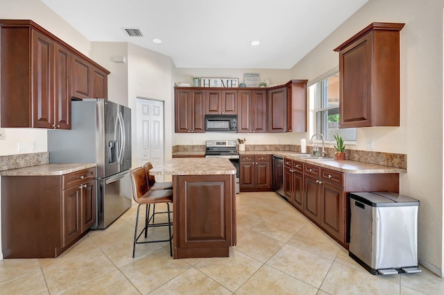 kitchen featuring sink, stainless steel appliances, a kitchen island, a breakfast bar, and light tile patterned flooring