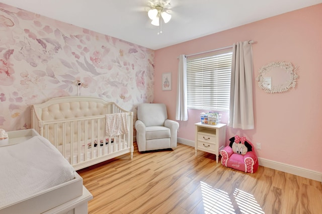 bedroom with light hardwood / wood-style floors, a nursery area, and ceiling fan