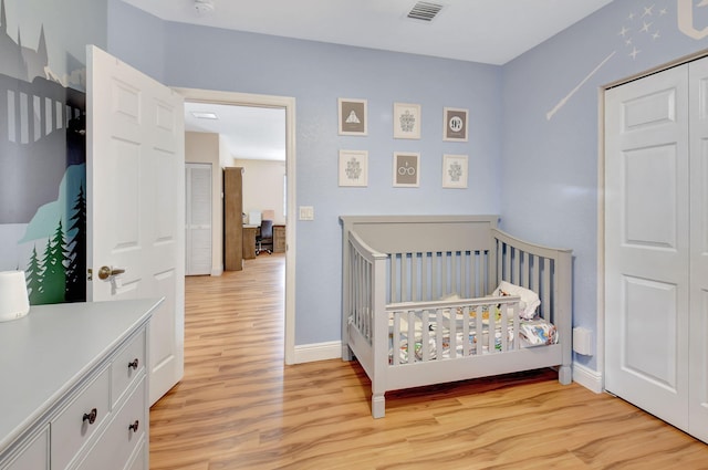 bedroom with a closet, light hardwood / wood-style flooring, and a nursery area