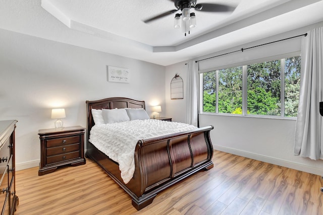 bedroom featuring ceiling fan, a tray ceiling, light hardwood / wood-style floors, and a textured ceiling