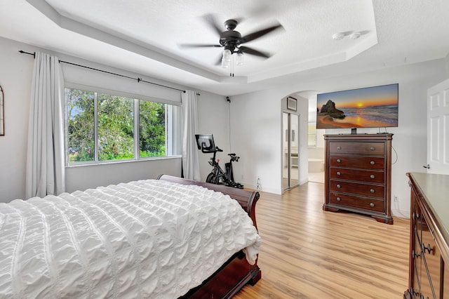 bedroom featuring ensuite bath, ceiling fan, a raised ceiling, light hardwood / wood-style flooring, and a textured ceiling