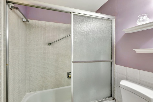 bathroom featuring shower / bath combination with glass door, toilet, and tile walls