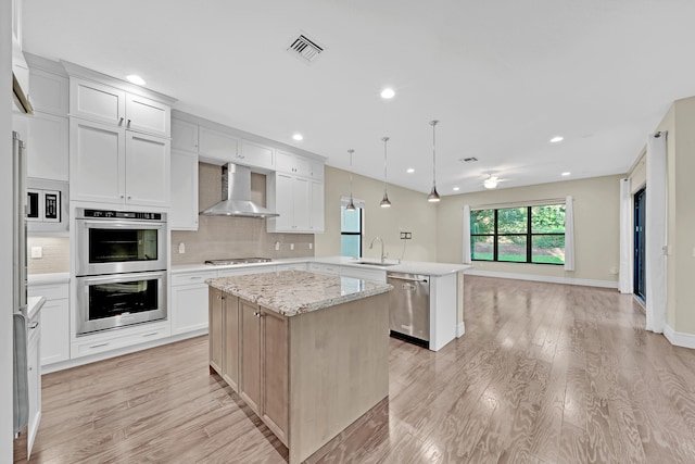 kitchen featuring stainless steel appliances, sink, wall chimney range hood, pendant lighting, and a center island