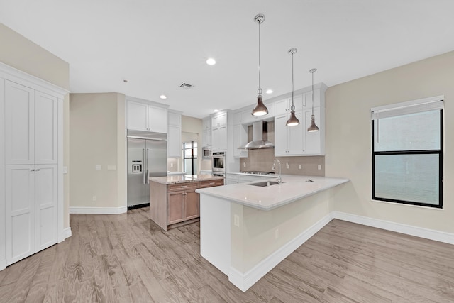 kitchen with pendant lighting, white cabinets, wall chimney exhaust hood, light wood-type flooring, and stainless steel appliances