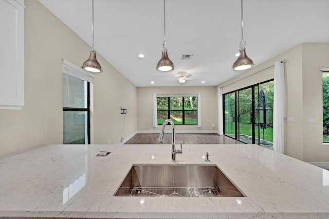 kitchen with light stone counters, sink, hardwood / wood-style floors, and decorative light fixtures