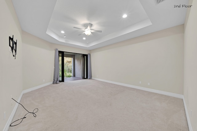 empty room with a tray ceiling, ceiling fan, and light colored carpet