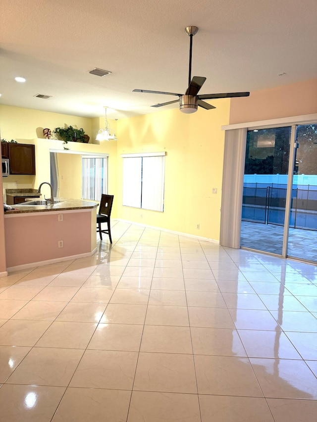 interior space featuring ceiling fan with notable chandelier, sink, light tile patterned floors, a textured ceiling, and kitchen peninsula