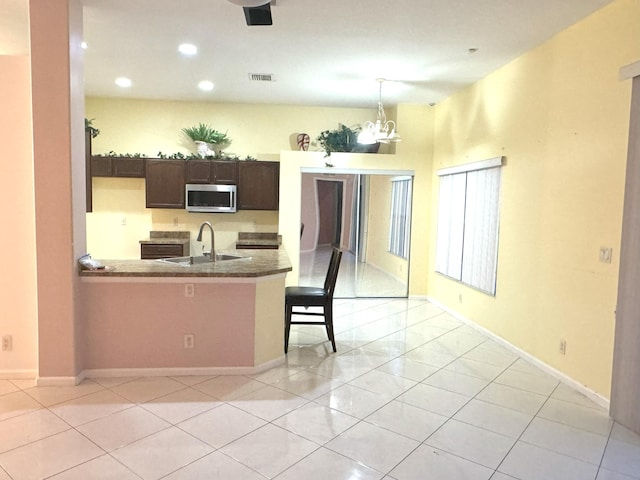 kitchen featuring kitchen peninsula, dark brown cabinetry, sink, and light tile patterned floors